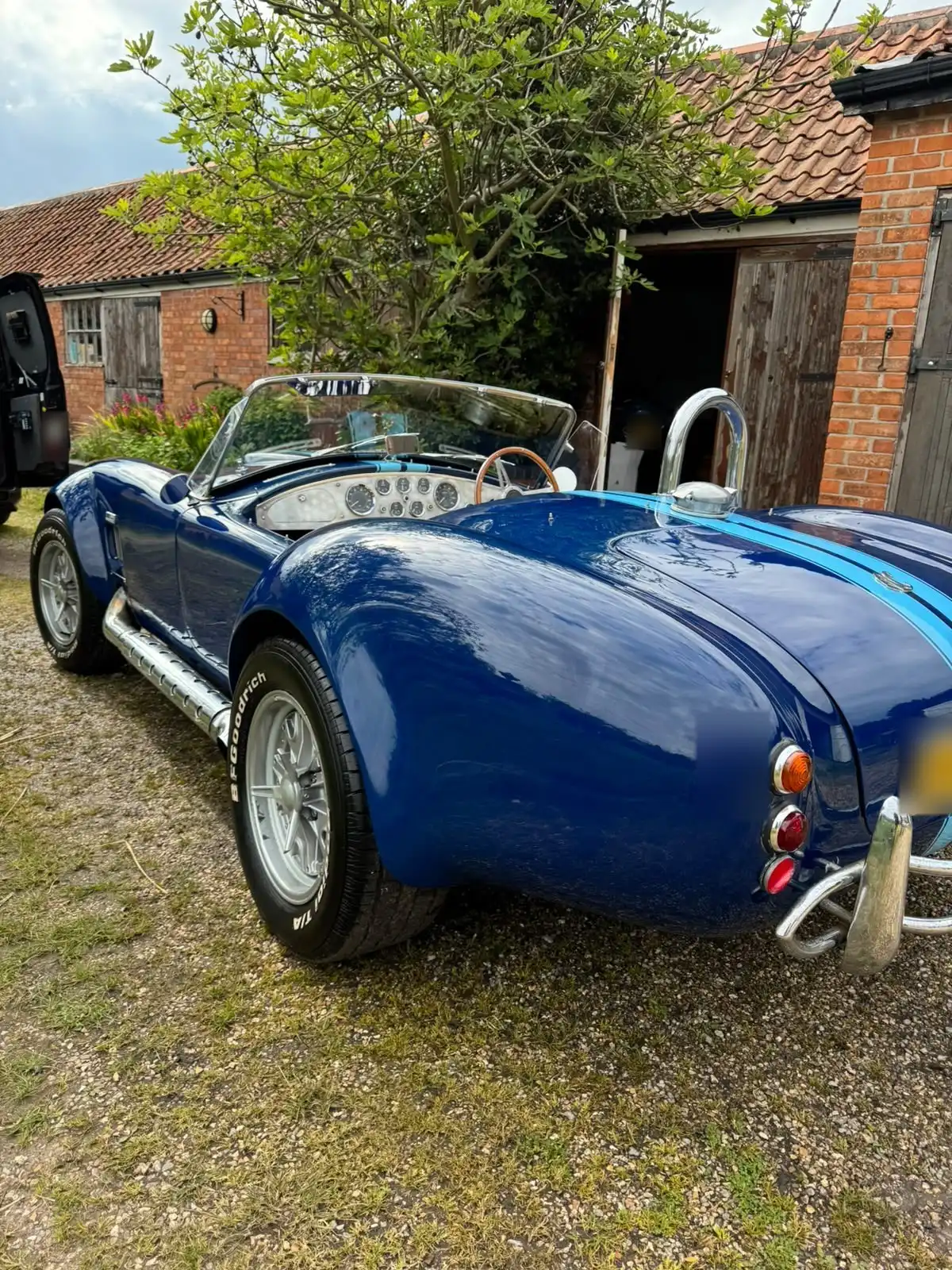 Blue AC Cobra replica from the rear quarter, showing the gloss on the rear wing, the chrome roll bar and the side exhaust