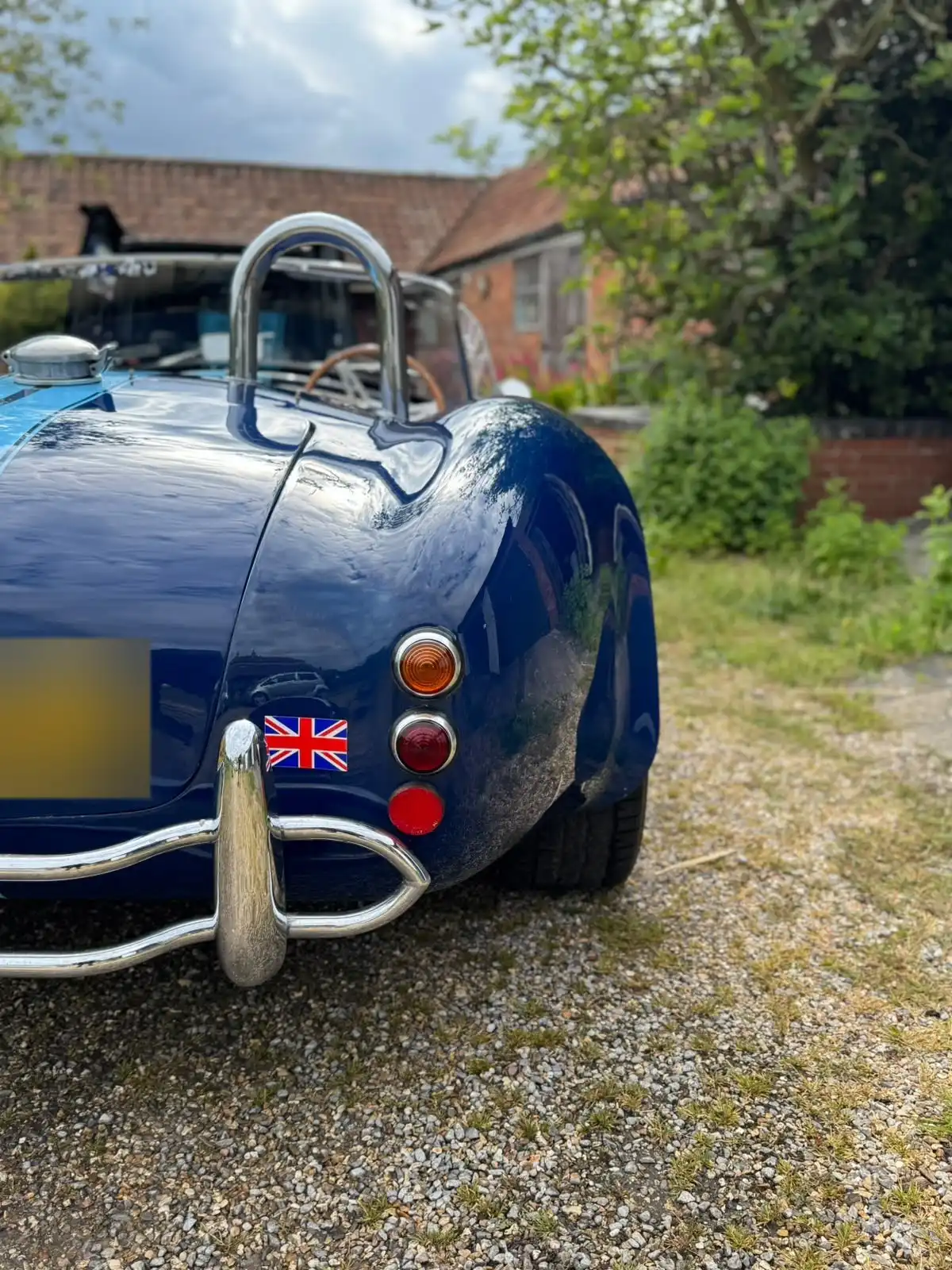 Rear of a blue AC Cobra replica, showing the reflections in the paint around the tail lights and chrome bumper