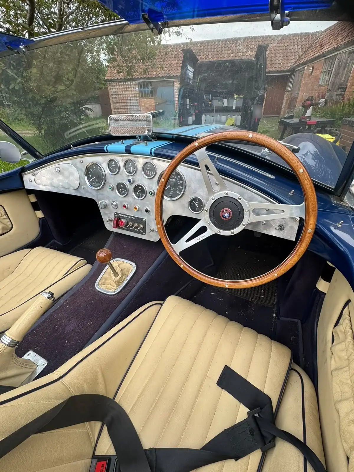 AC Cobra replica cockpit, showing the wood rim steering wheel, the engine turned dashboard and cream leather seats