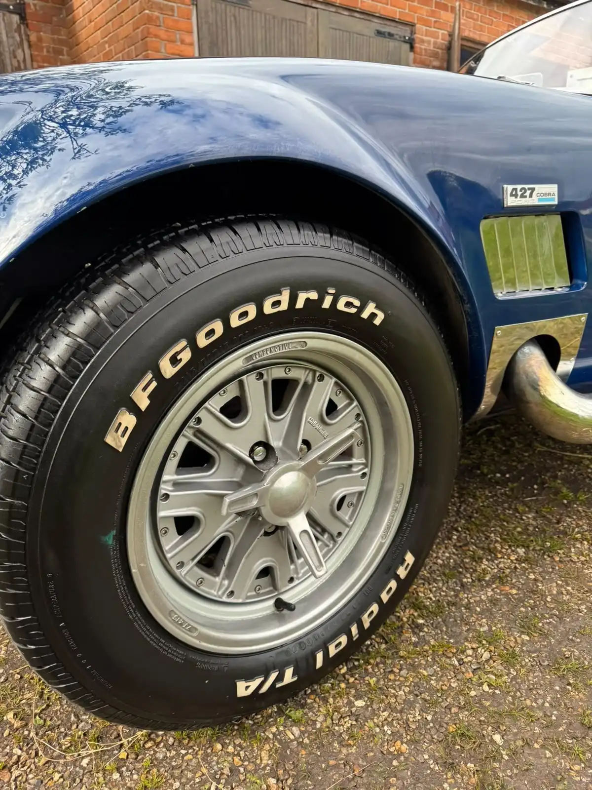 Front wheel and wing of a blue AC Cobra replica, with the 427 Cobra badge, side vent and chrome exhaust