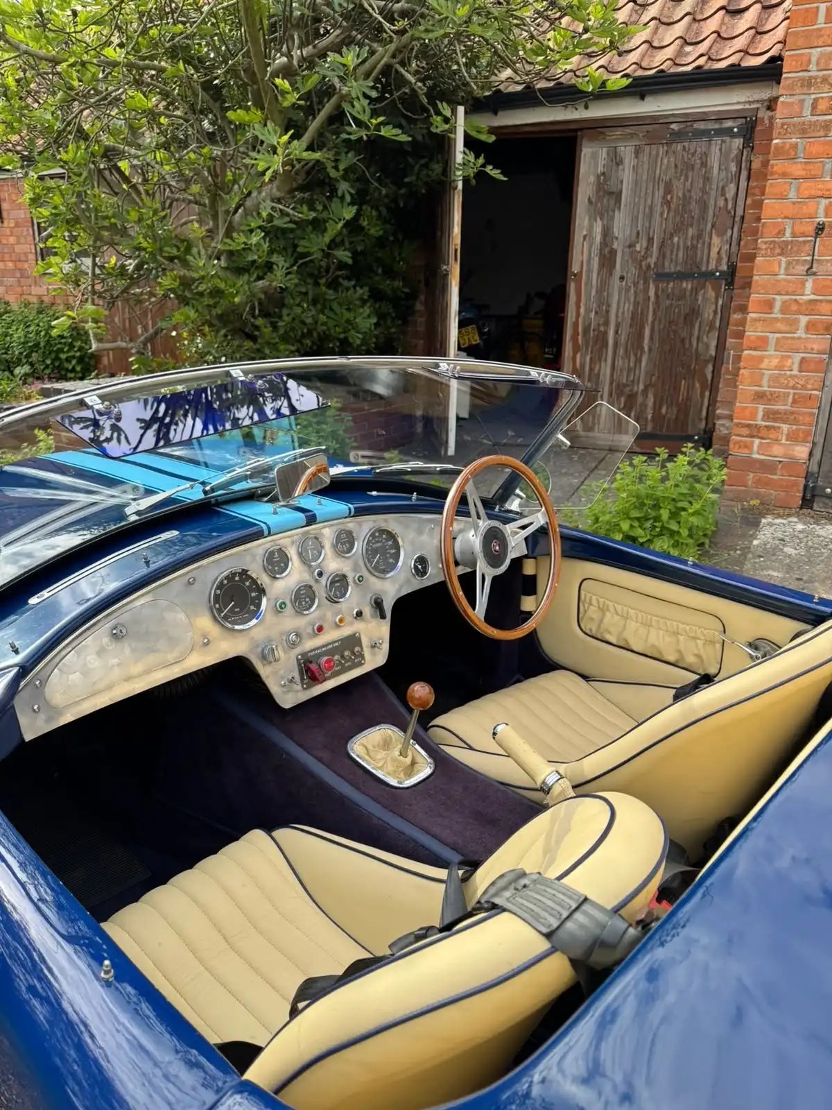 Cockpit of a blue AC Cobra replica seen from above, showing cream leather seats and the dashboard