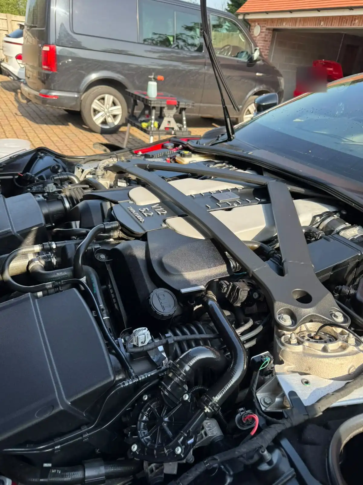 Aston Martin DB11 engine bay with the bonnet open, showing the finish on the V12 engine cover and strut brace