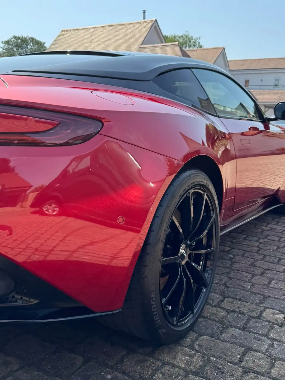 Rear quarter of a red Aston Martin DB11, close enough to show the depth of the paint