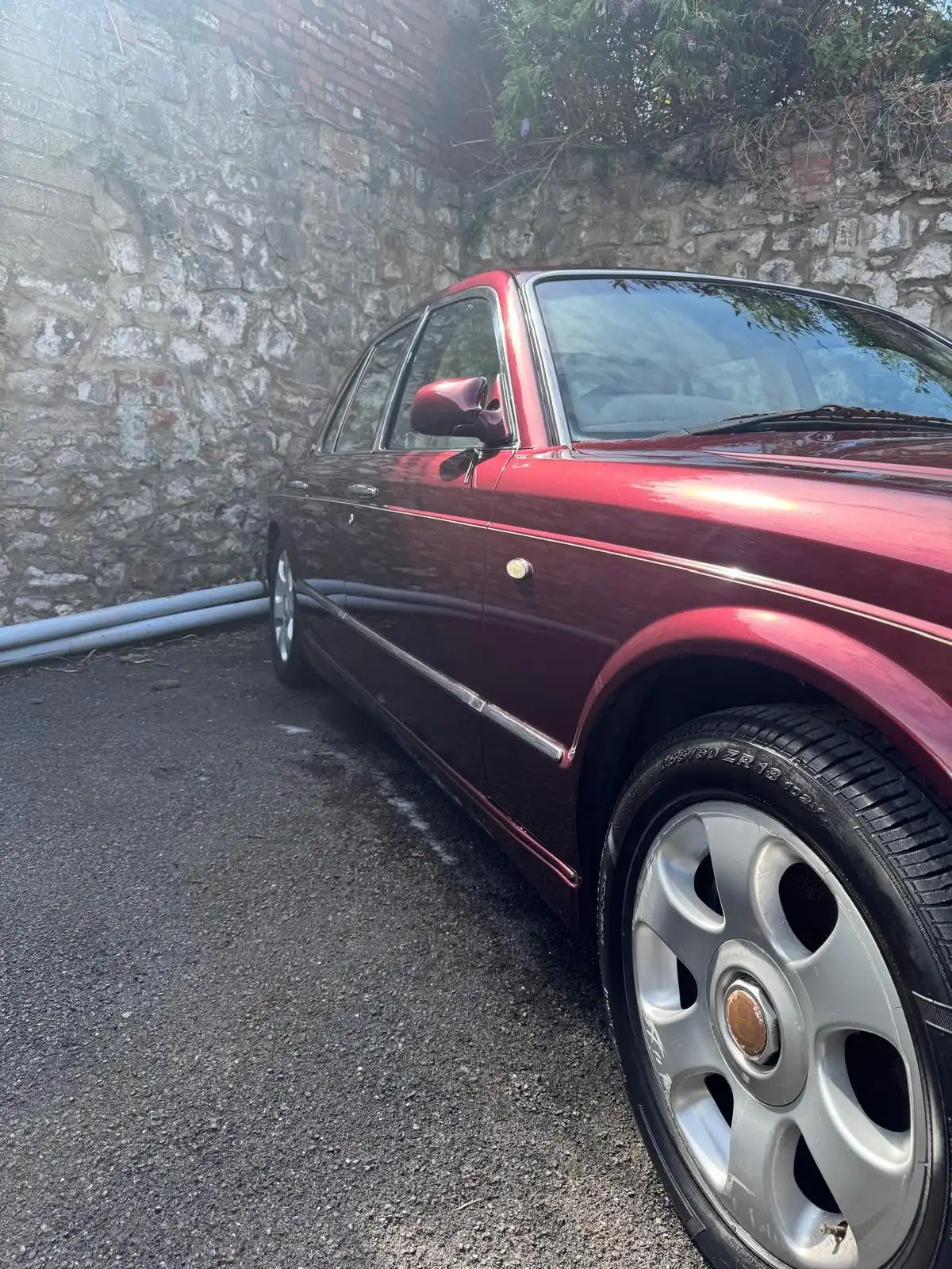 Side of a burgundy Bentley Arnage from low down, showing the gloss along the doors and the silver wheel