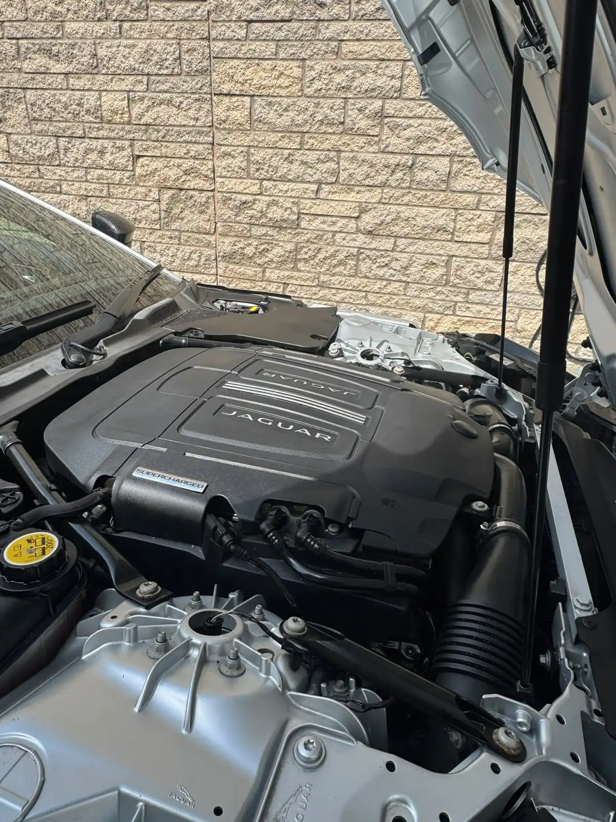 Supercharged Jaguar engine bay with the bonnet open and the engine cover clean, an example of an engine bay