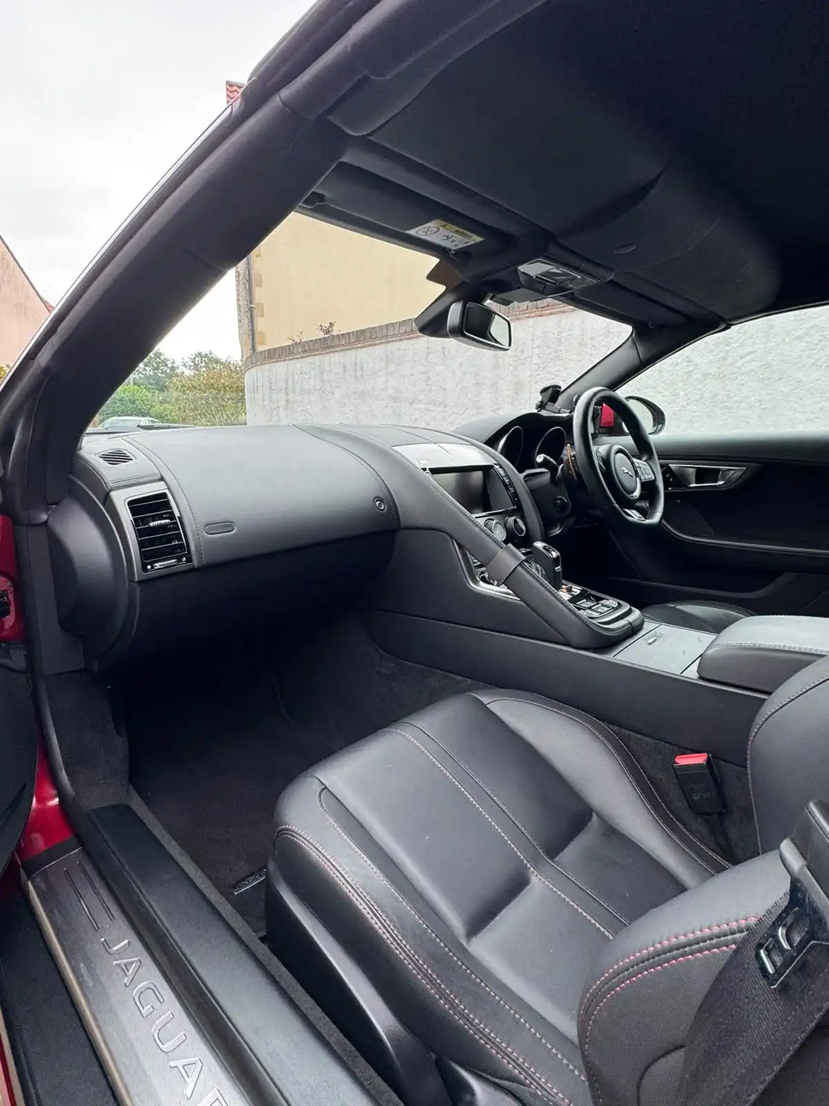 Jaguar F-Type convertible cabin from the passenger door, showing the dashboard, black leather seats and carpets