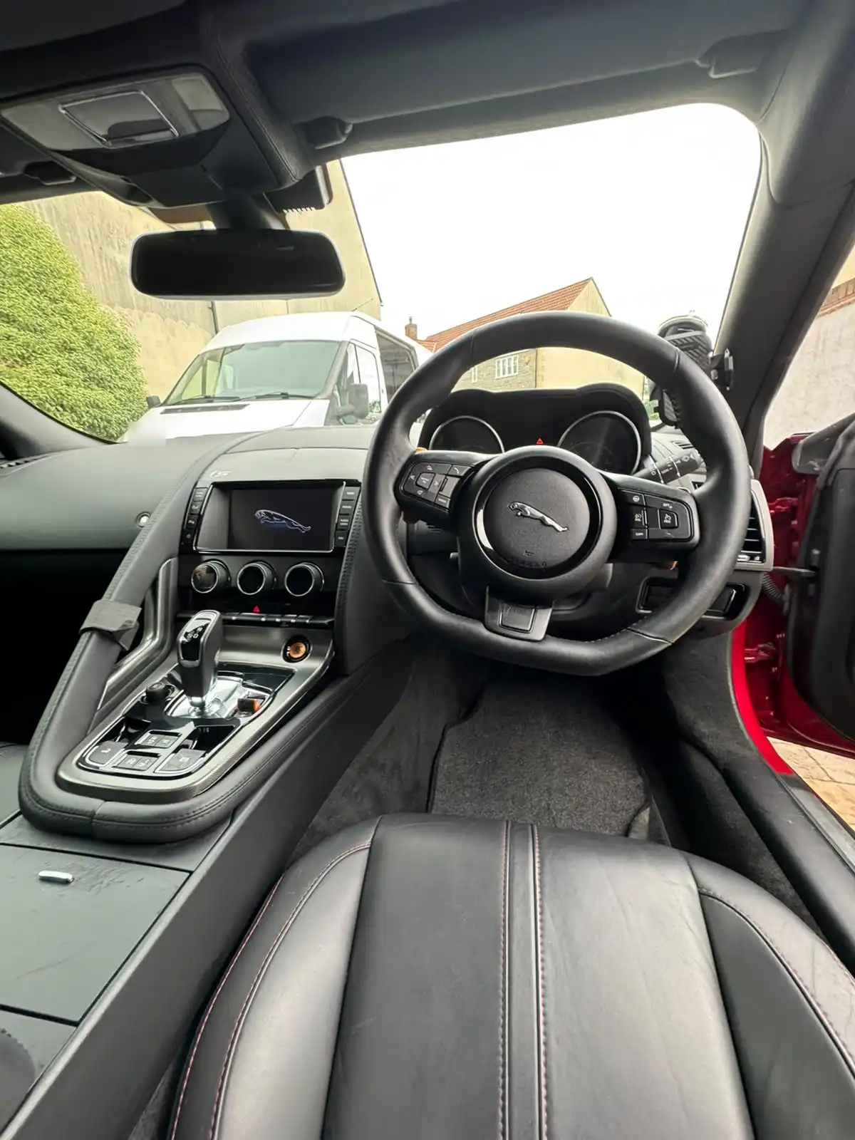 Jaguar F-Type convertible cabin from the driver side, showing the steering wheel, centre console and black leather seat with red stitching