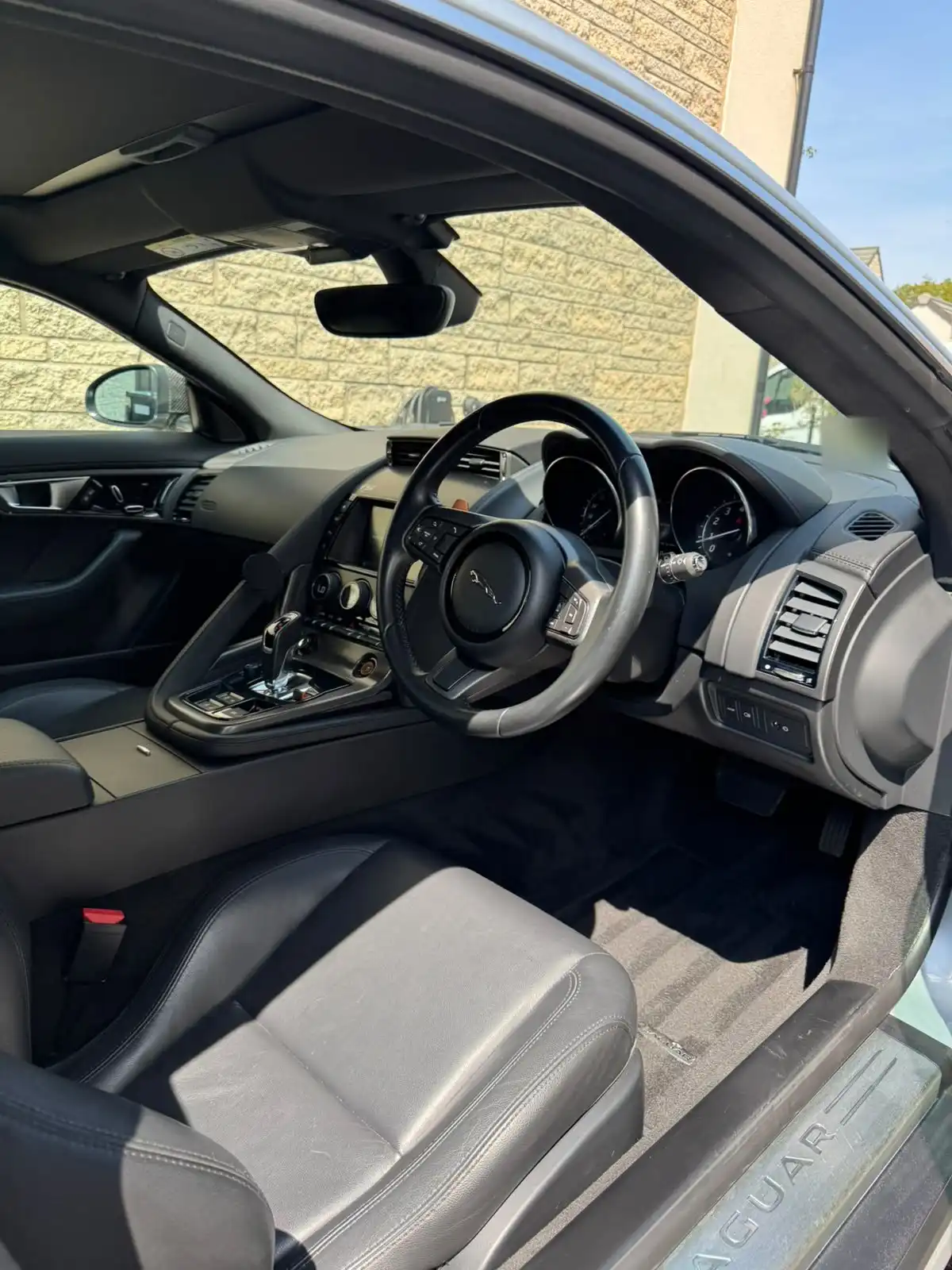 Jaguar F-Type coupe cabin seen through the open driver door, showing the black leather seat, steering wheel and dashboard