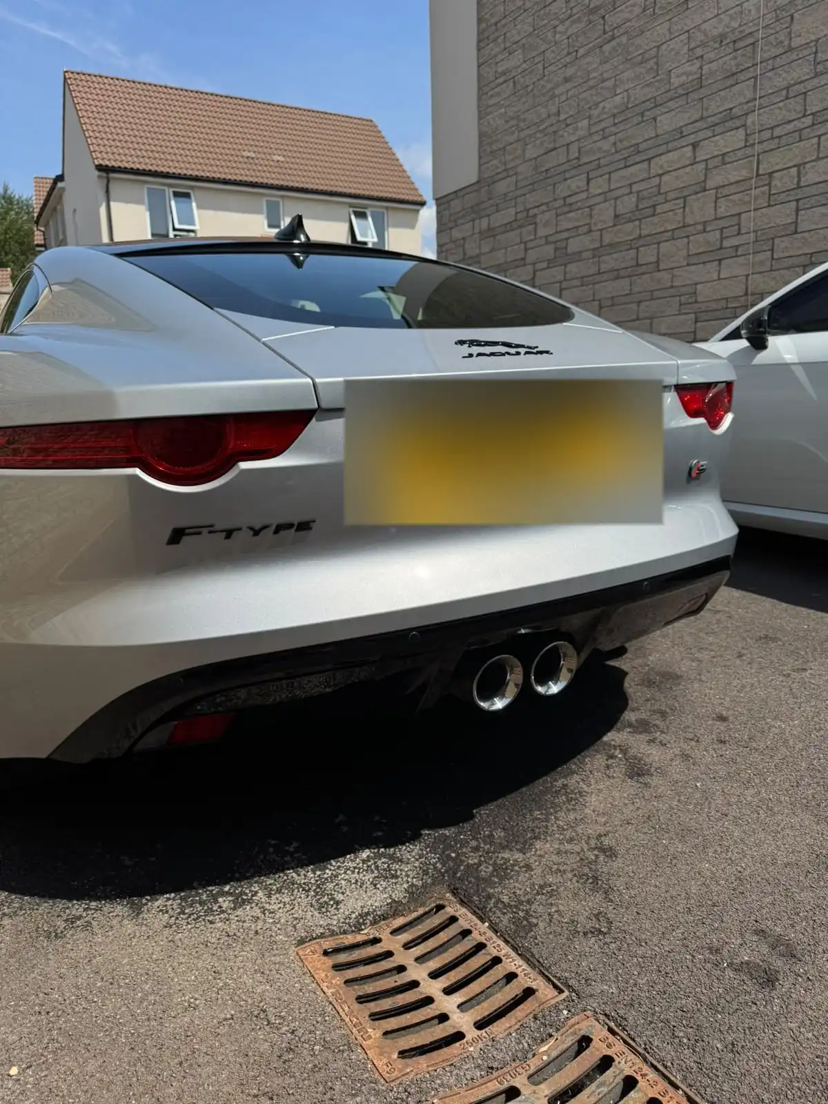 Rear of a silver Jaguar F-Type coupe with its twin exhaust tips, showing the reflections across the boot lid and bumper