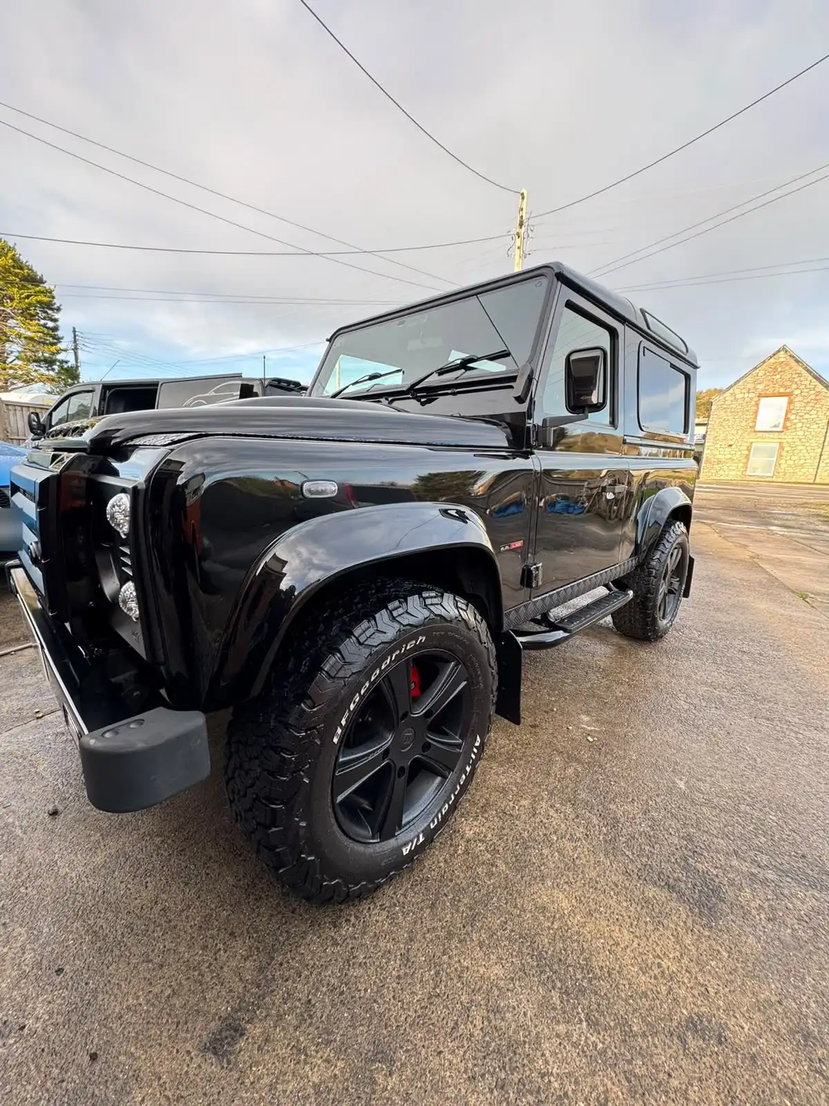 Black Land Rover Defender from the front three quarter, showing gloss on the black paint and the black wheels with red brake calipers