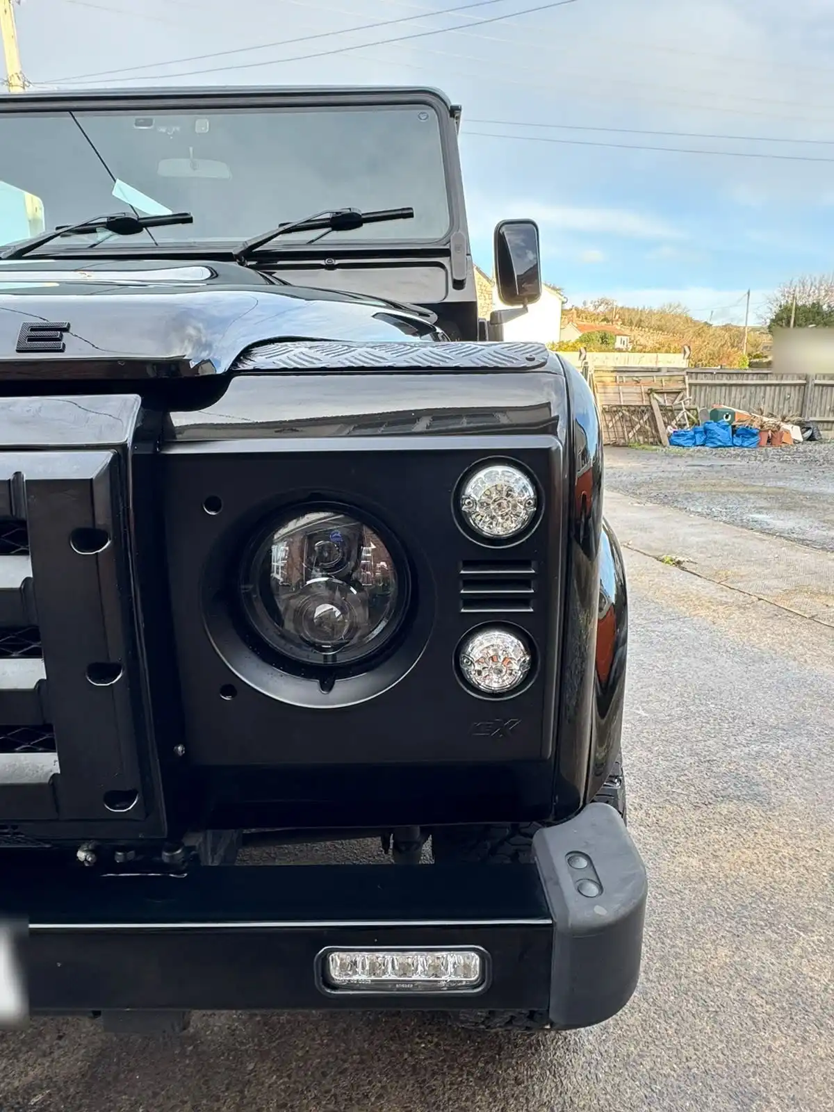 Front of a black Land Rover Defender, close enough to show the gloss on the wing, the headlamp surround and the chequer plate