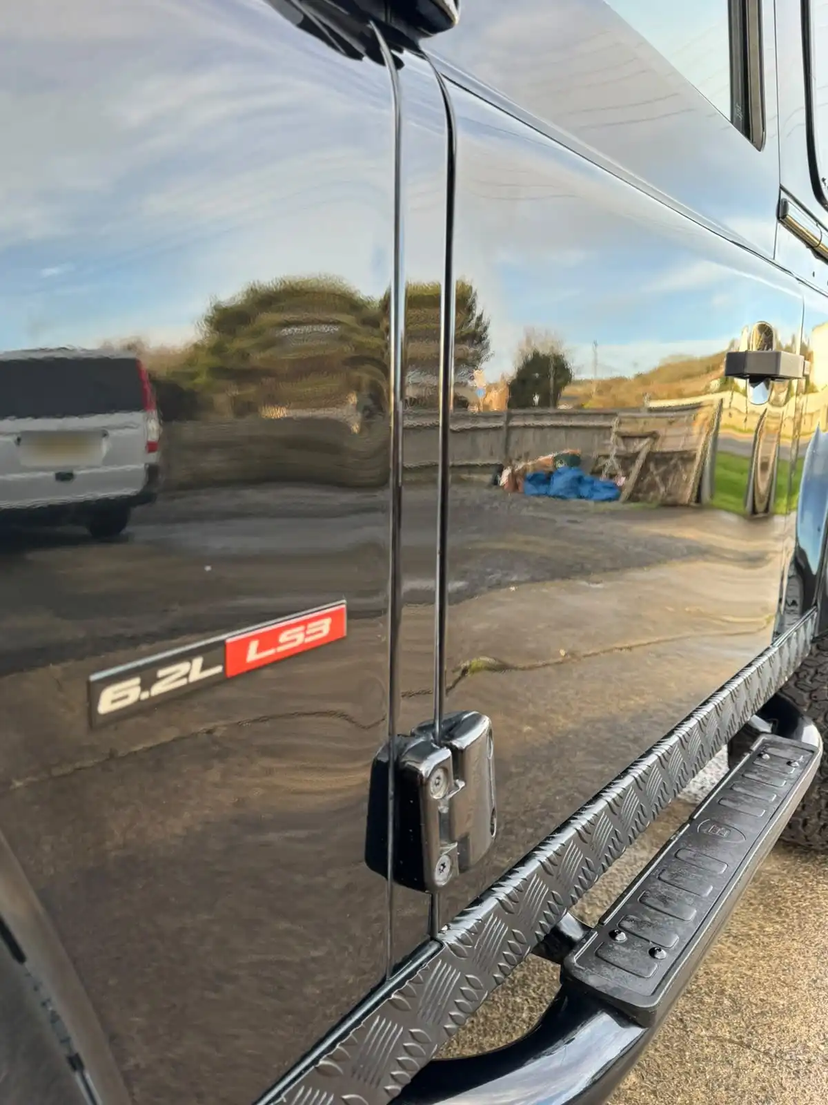 Side of a black Land Rover Defender with a 6.2L LS3 badge, showing a mirror like reflection in the door