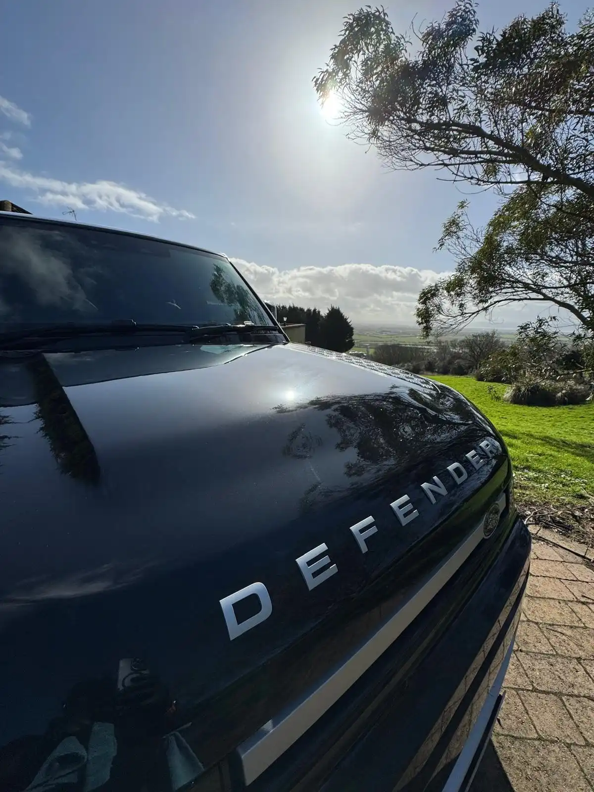 Defender script on the bonnet of a black Land Rover Defender, with the sky reflected in the paint