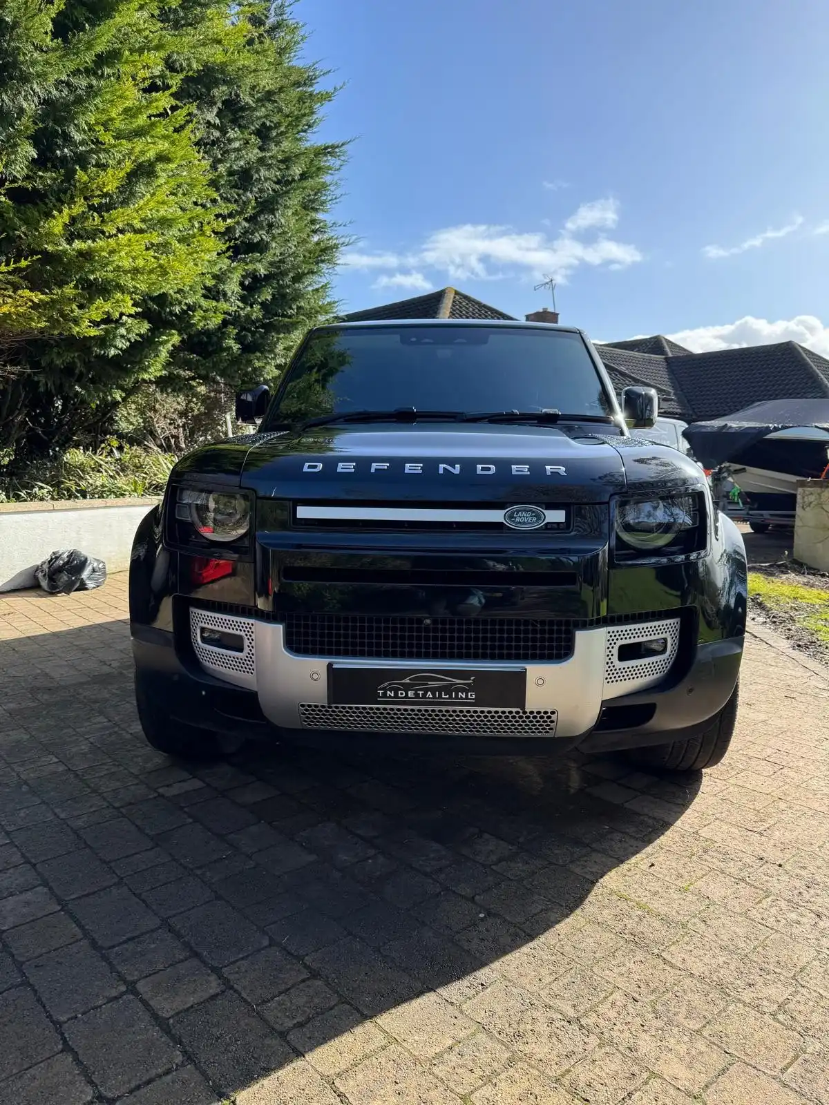 Black new shape Land Rover Defender seen head on, showing the gloss on the bonnet and a TNDetailing plate