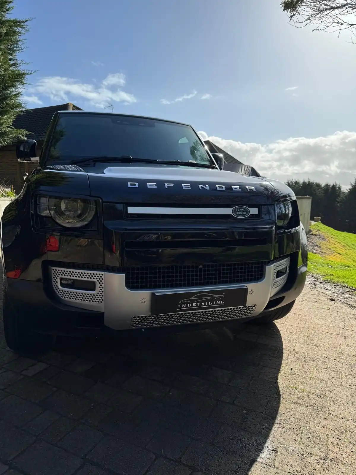 Close front view of a black new shape Land Rover Defender, showing the grille, headlamps and the shine on the bonnet