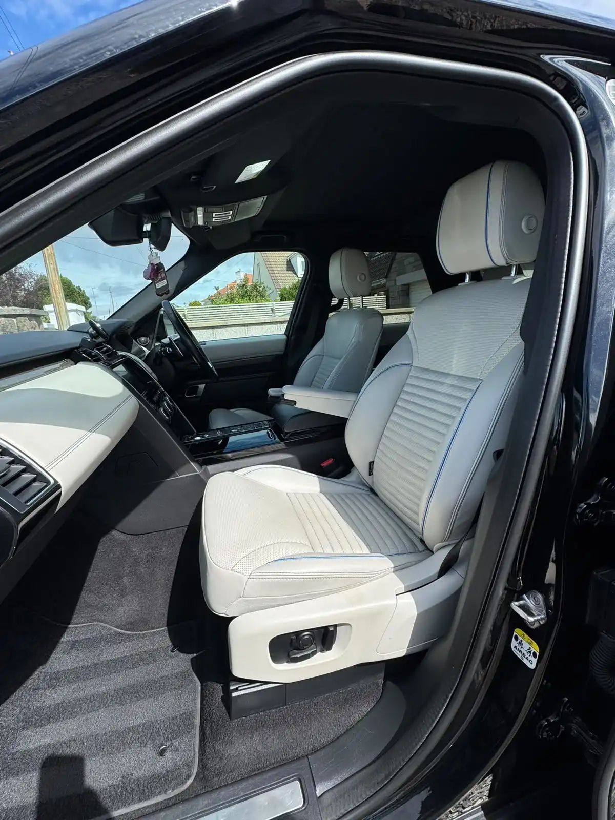 Land Rover Discovery front seats seen through the open passenger door, showing white leather with blue piping
