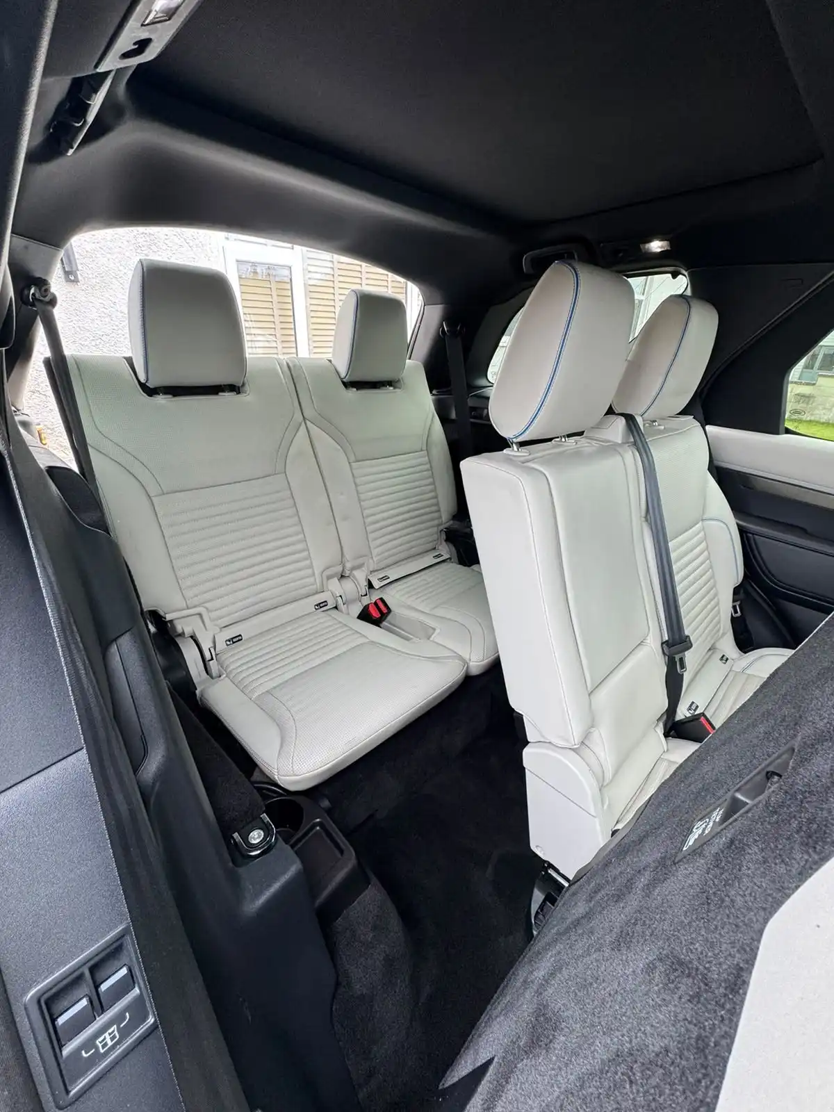 Second and third row seats of a Land Rover Discovery seen from the boot, all in white leather with blue piping