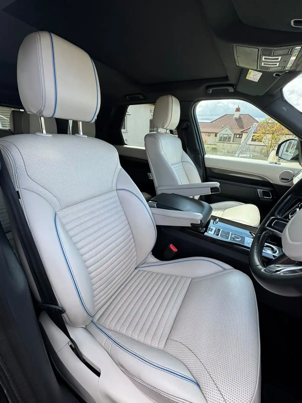 Close view of a white perforated leather front seat with blue piping in a Land Rover Discovery, showing the condition of the leather