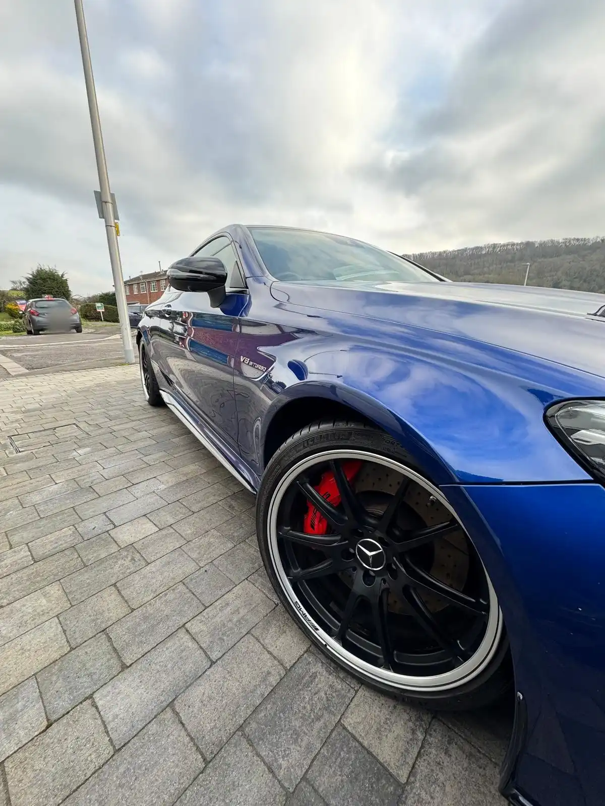 Side of a blue Mercedes-AMG C63 coupe from low down, showing the black wheel, red caliper and the gloss along the door