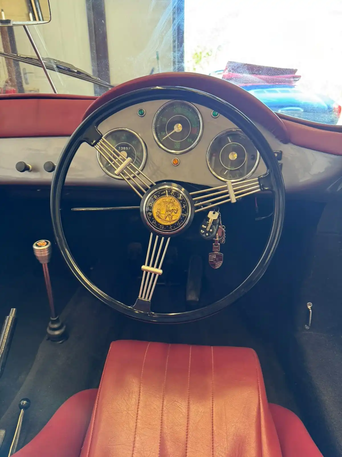 Cockpit of a grey Porsche 356 style speedster, showing the banjo steering wheel, the round gauges and the red seat