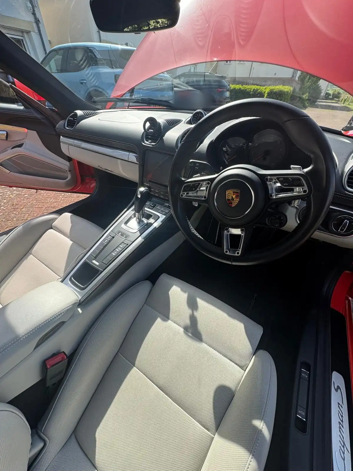 Porsche Cayman S cabin seen through the open driver door, showing the steering wheel, dashboard and light grey seats