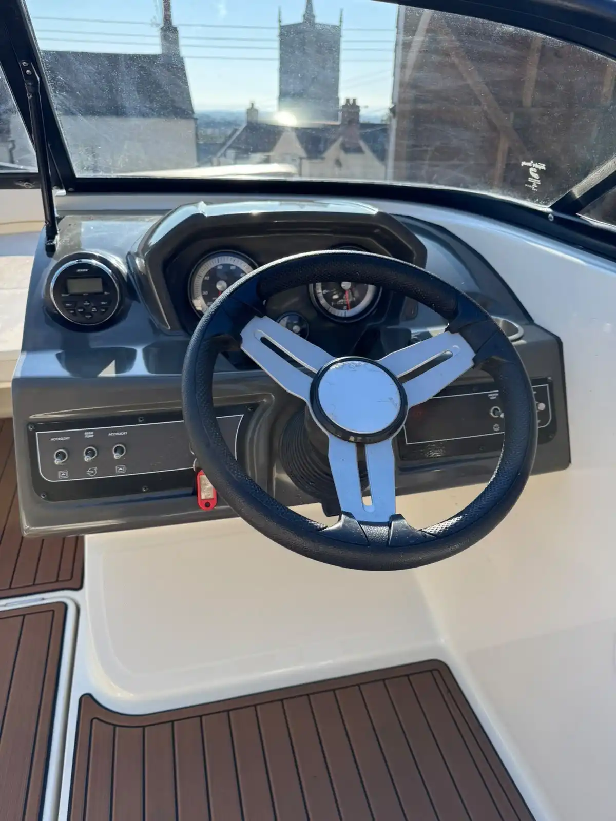 Close up of a speedboat helm, with the steering wheel and dashboard above a wood effect deck