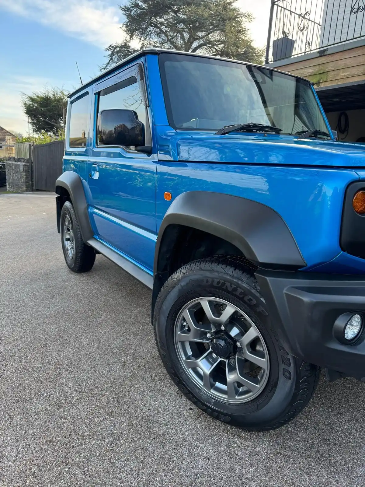 Front wing and wheel of a blue Suzuki Jimny from low down, showing the clean alloy and tyre