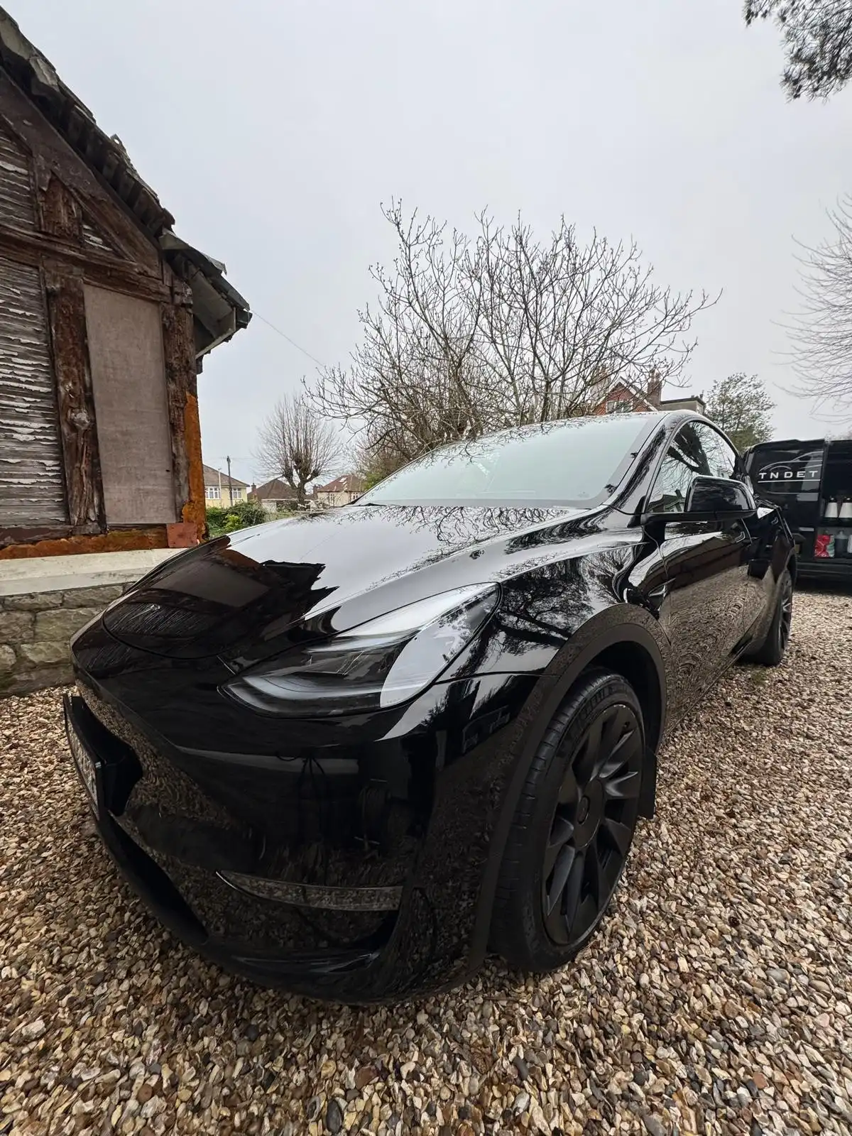 Black Tesla Model Y from the front quarter, showing the reflections across the bonnet and wing