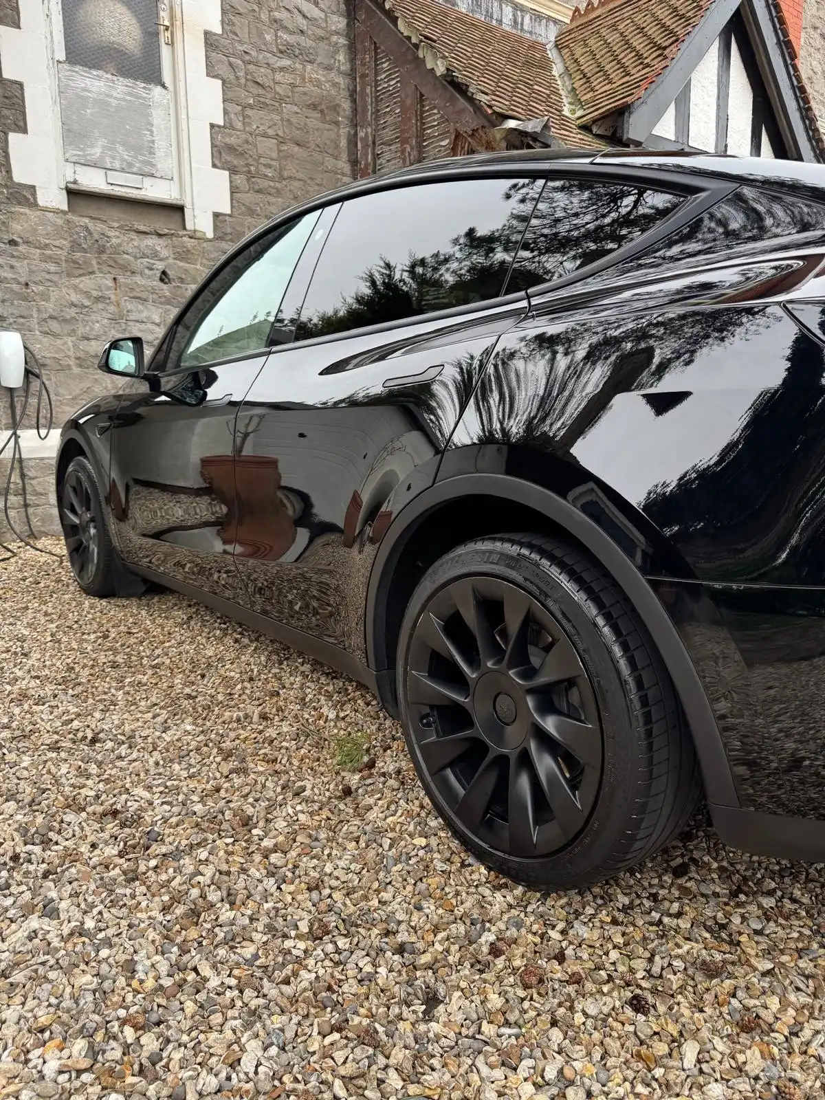 Side of a black Tesla Model Y, showing the sky reflected along the doors