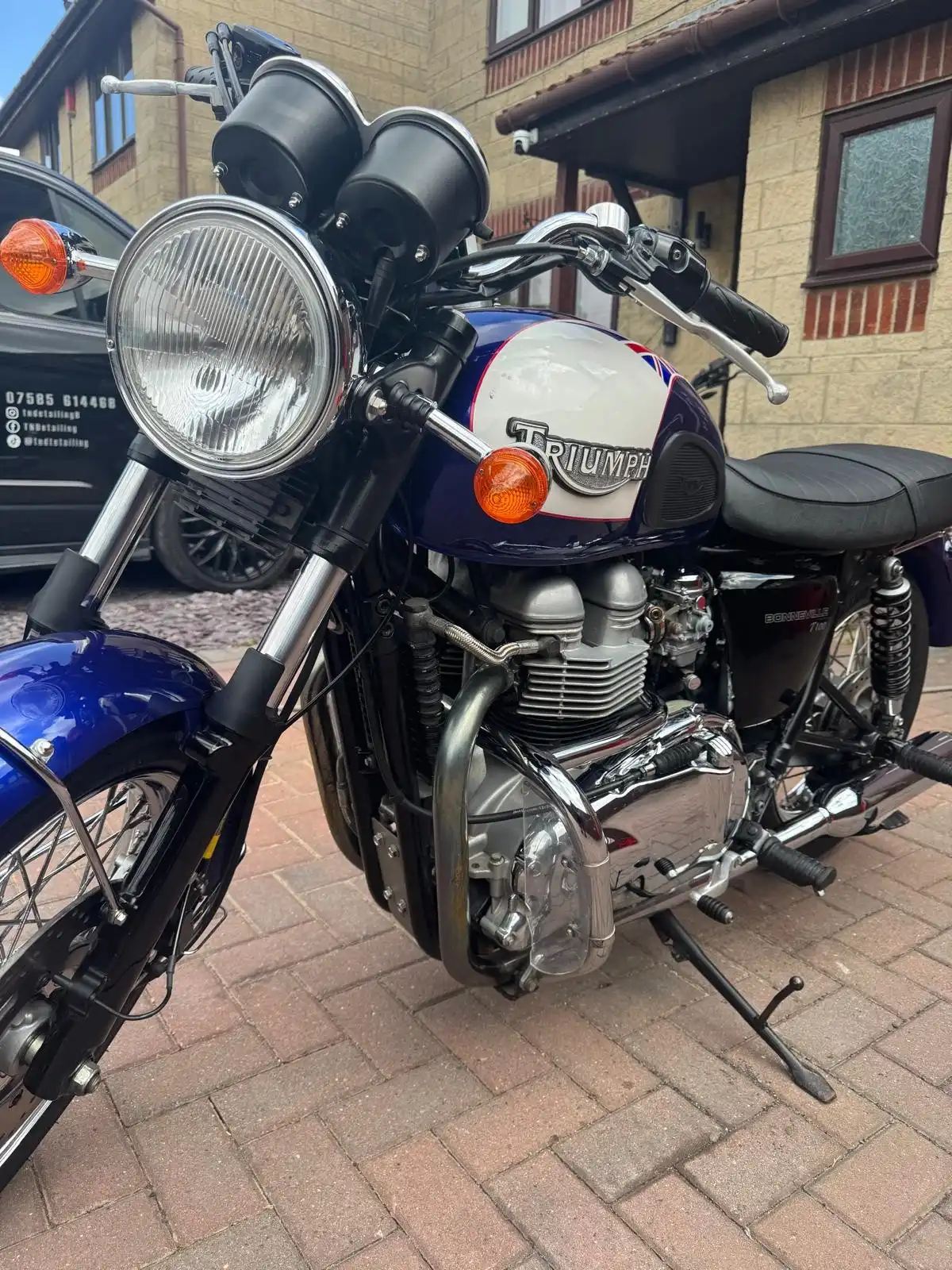 Blue and white Triumph Bonneville T100 from the front, showing the chrome headlamp, tank badge and engine
