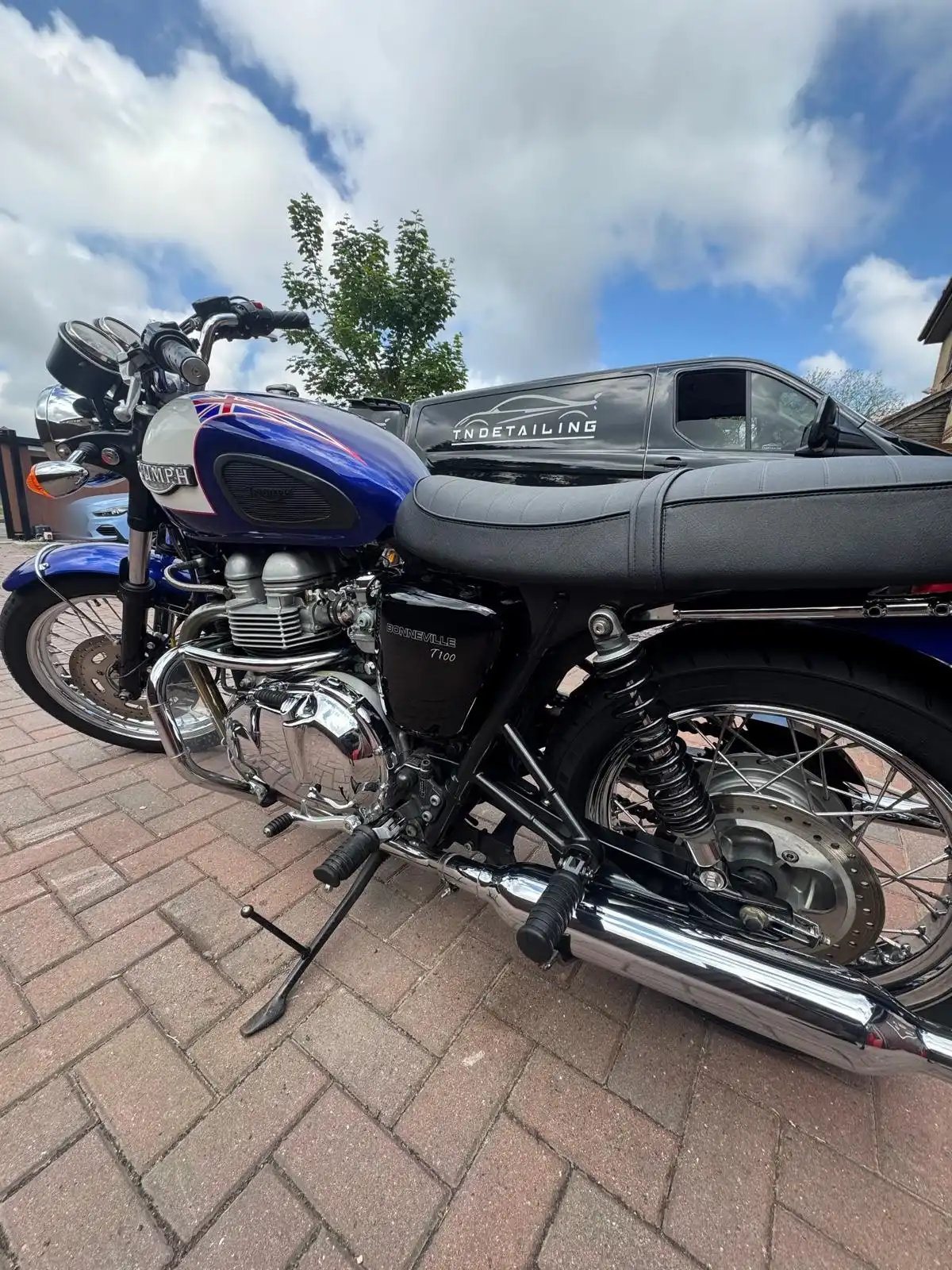 Triumph Bonneville T100 from the side, showing the blue tank, chrome engine covers and exhaust
