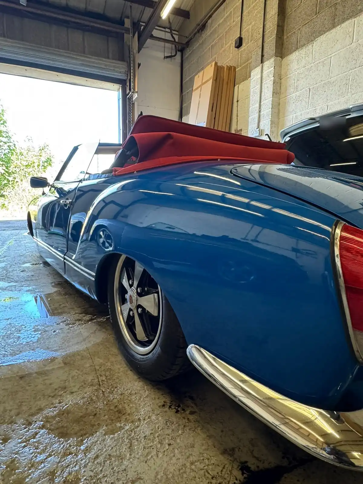 Blue VW Karmann Ghia convertible from the rear quarter with the red hood folded, showing the reflections along the rear wing