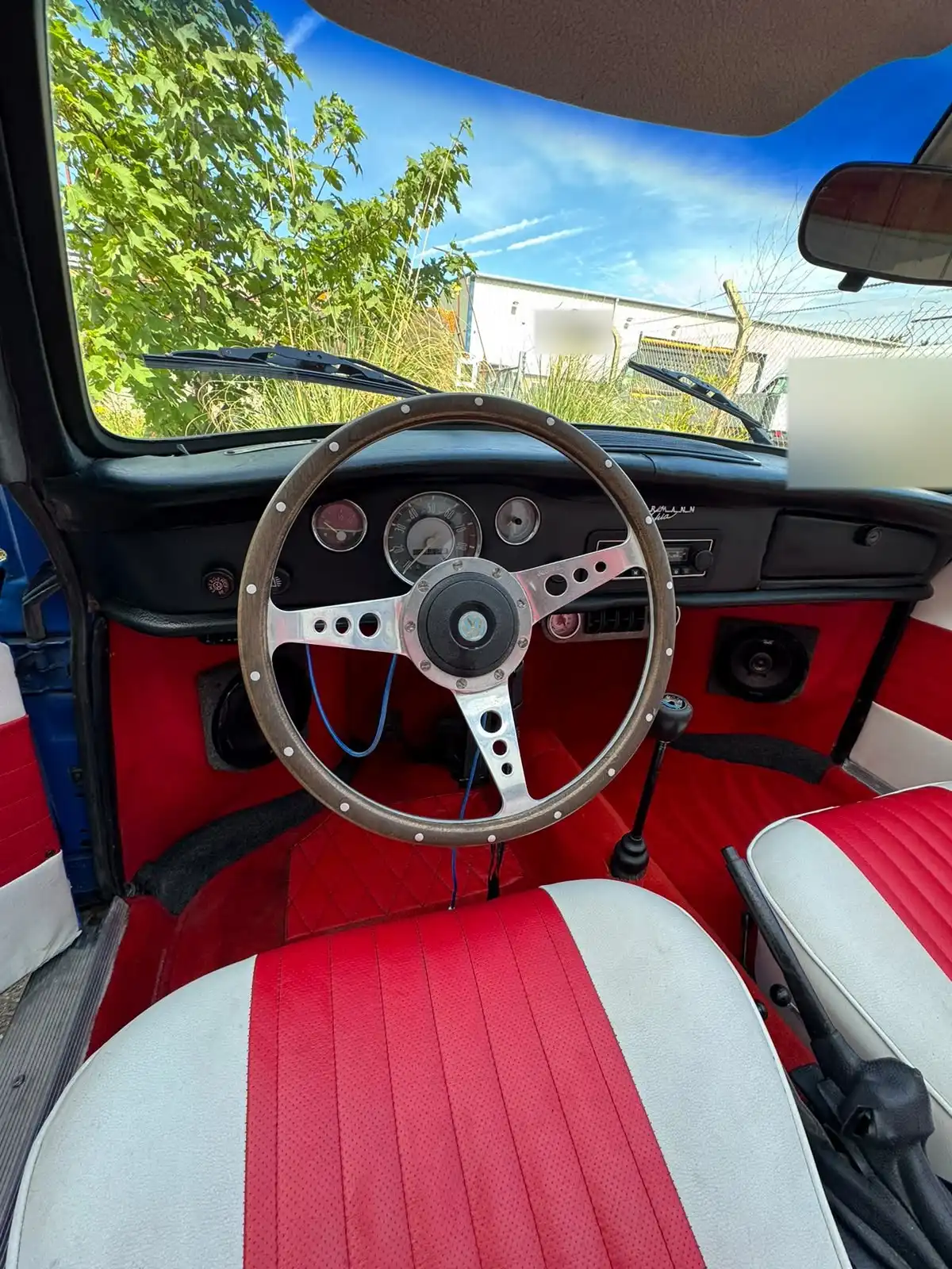 VW Karmann Ghia dashboard with a wood rim steering wheel and round gauges, above red carpets and red and white seats