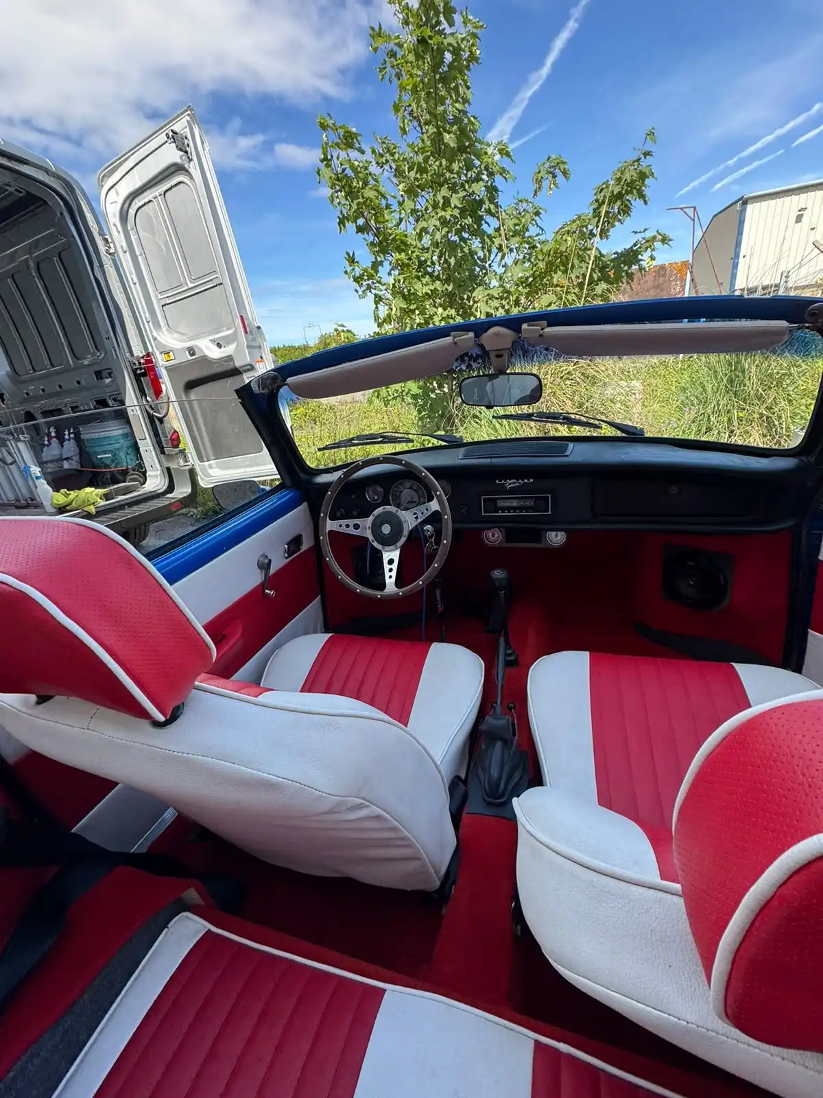 Inside a VW Karmann Ghia with the roof down, showing the red and white seats, red carpets and dashboard