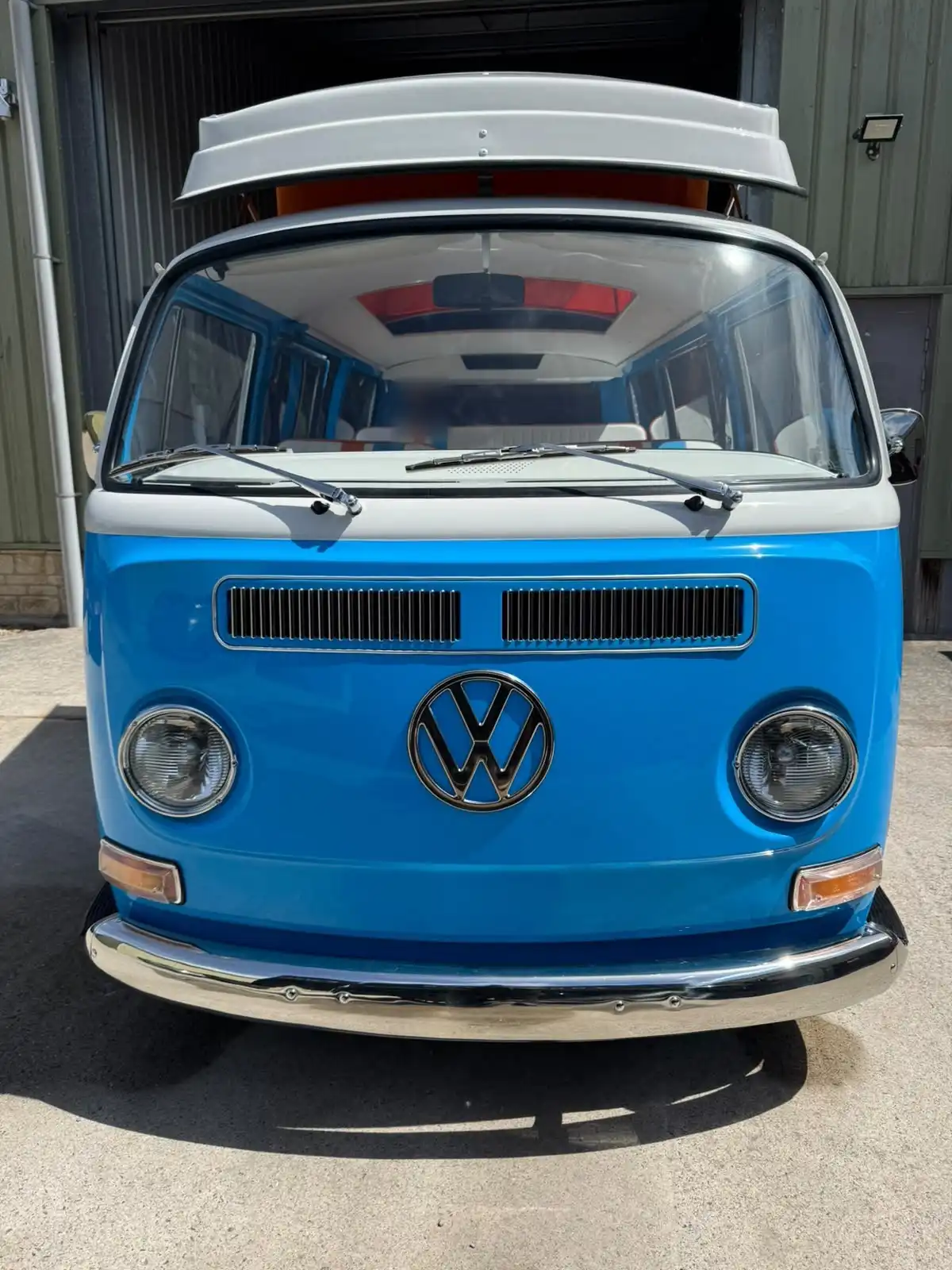Blue and white classic VW T2 camper seen head on, showing glossy paintwork and bright chrome
