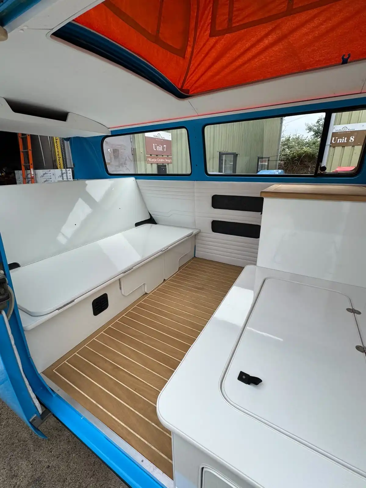 Inside a classic VW T2 camper, white seating and units over a wood effect floor, an example of interior work
