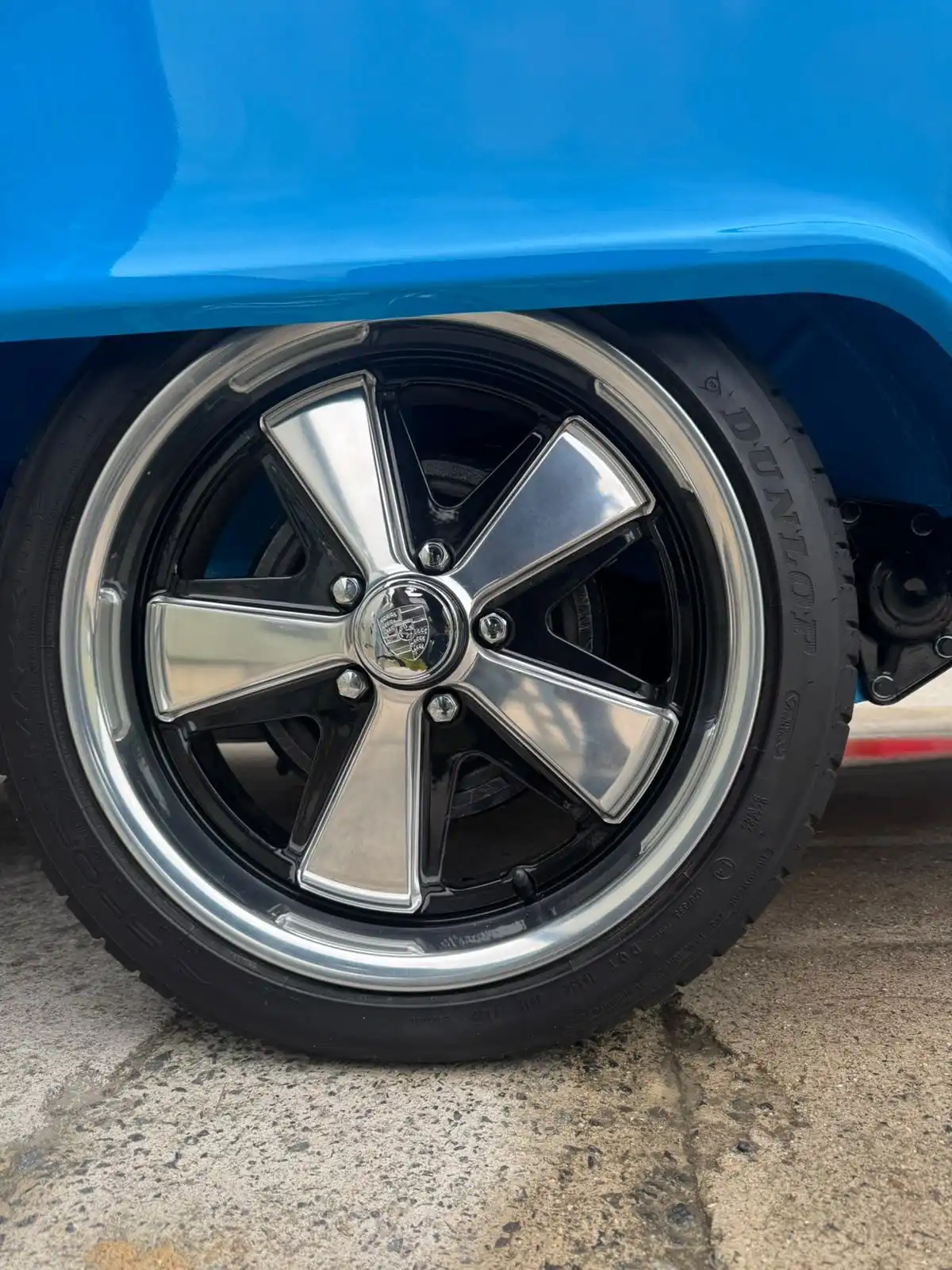 Close up of a five spoke alloy wheel on a blue VW T2 camper, showing the shine on the spokes and rim