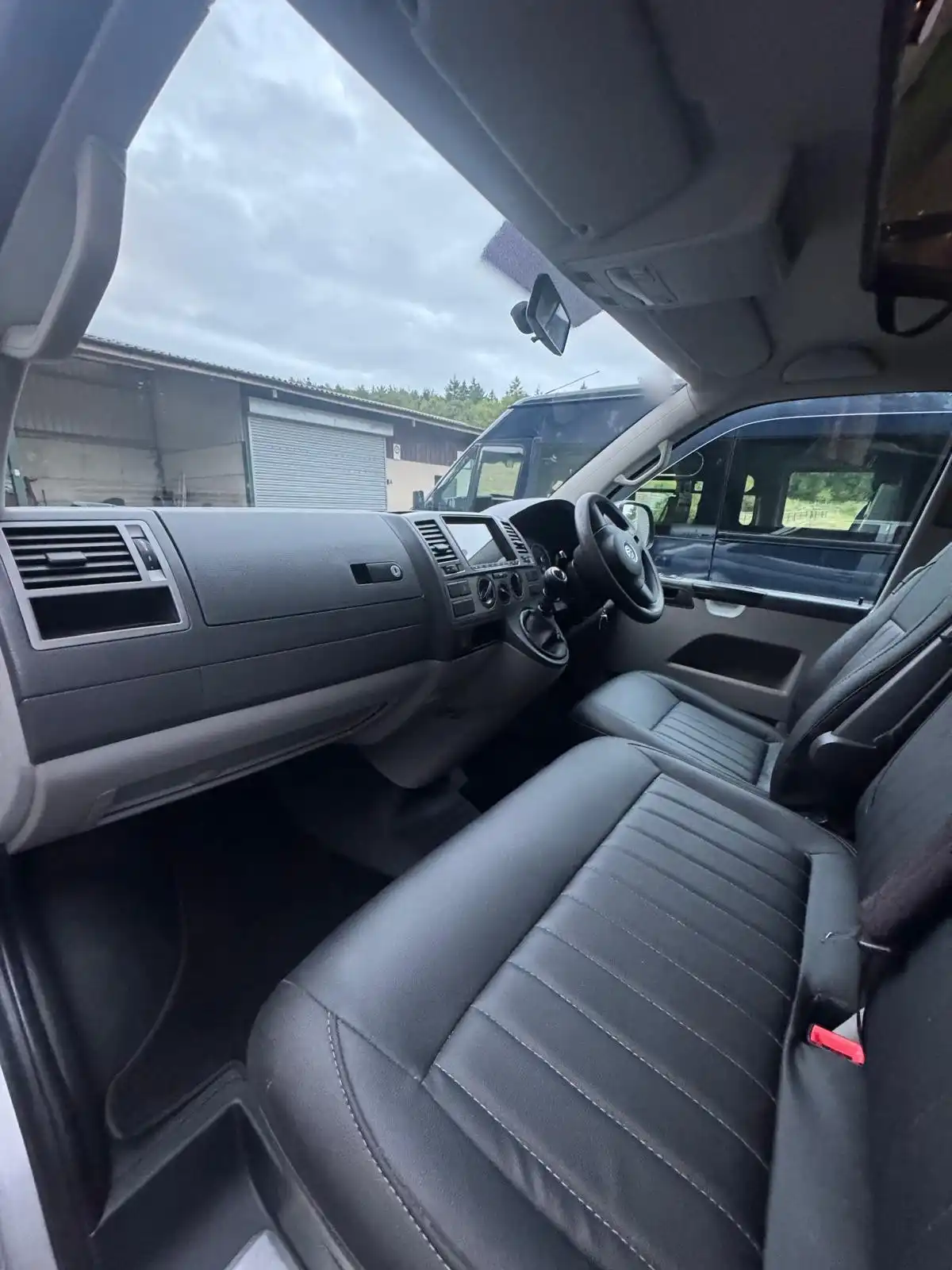 Cab of a VW Transporter camper seen through the passenger door, showing the dashboard and black leather seats